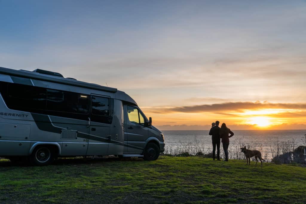 Couple and dog faces the water next to their Class B Motorhome